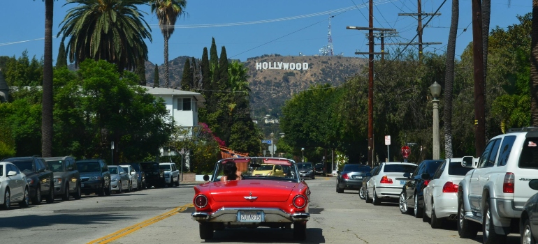  Red vintage convertible driving toward the Hollywood sign on a sunny day—movers Hollywood CA ready to take you there.