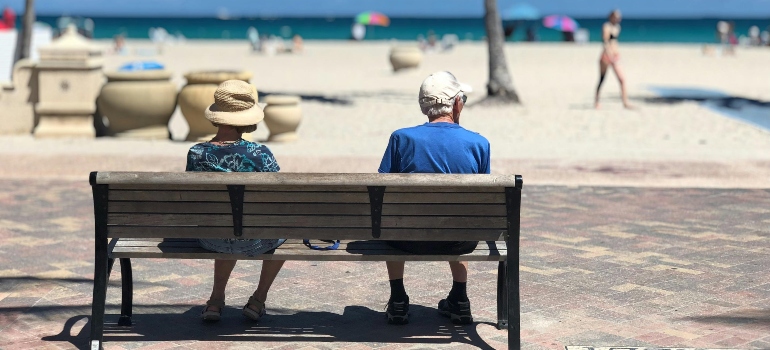 Elderly couple sitting on a bench, enjoying a quiet moment on a sunny beach.