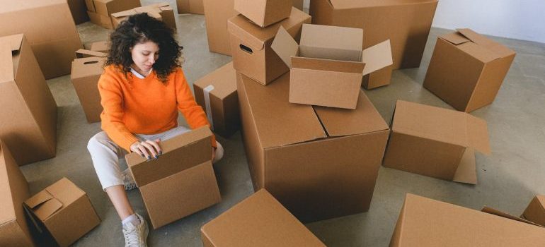 Young relocating lady packing carton boxes sitting on floor before booking one of the best moving companies Rancho Cucamonga CA