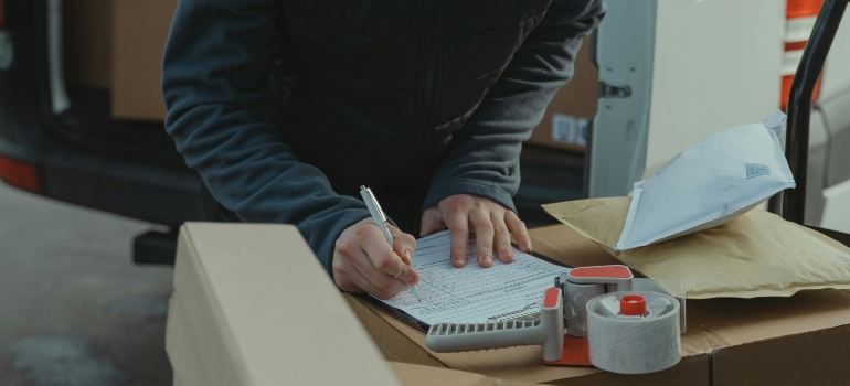 A man is writing a notes about packages on the carton box.