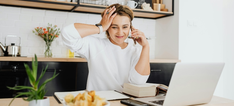Woman Sitting in Front of a Laptop and Talking on the Phone