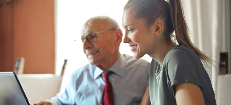 Young woman helping senior man with payment on Internet using laptop