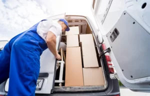 Worker in blue uniform loading cardboard boxes into the back of a white moving vehicle.