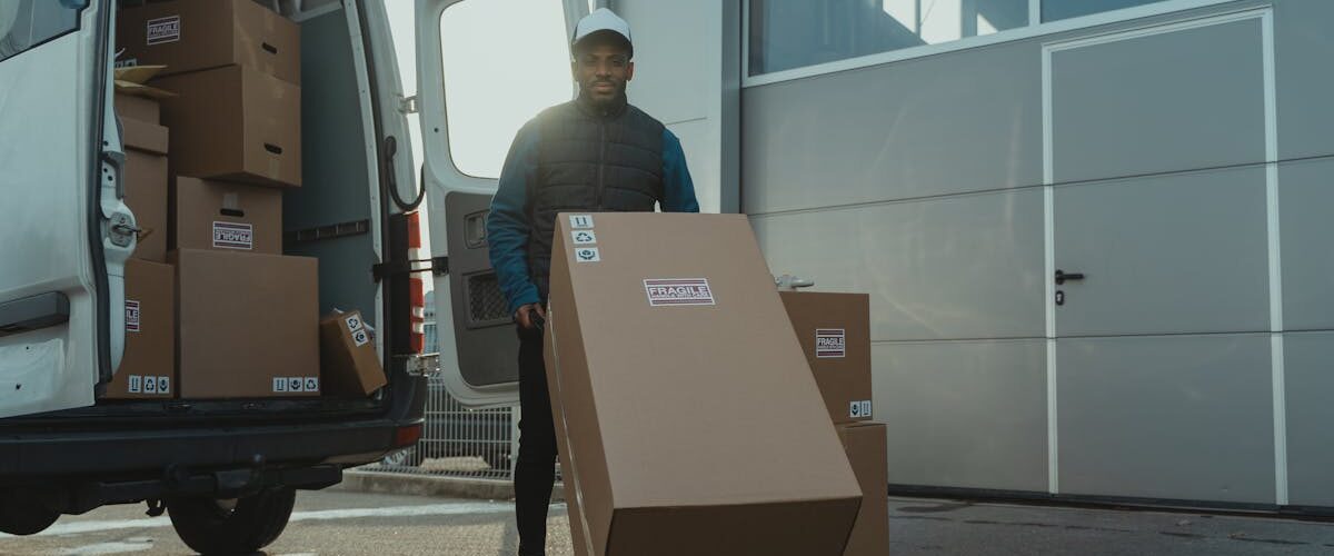 Person maneuvering a cart with a large box beside a delivery van full of stacked boxes, illustrating warehouse moving in LA.