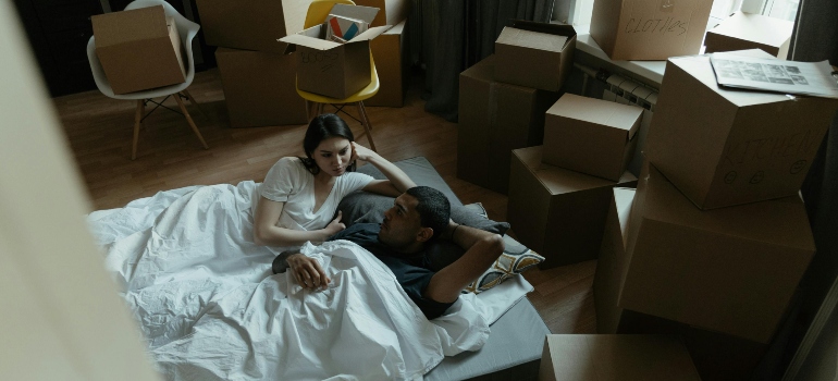 Couple lying on a mattress in a room filled with moving boxes.