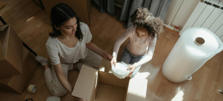 Mother and child carefully wrapping dishes with bubble wrap while packing moving boxes.