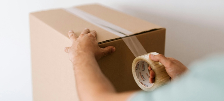 Close-up of a person applying clear packing tape to seal a cardboard moving box.