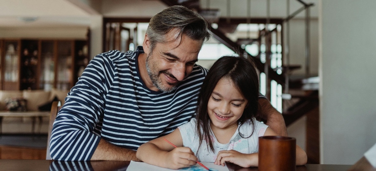 Father and daughter happily painting together at a table inside their home.