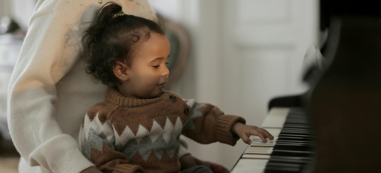 A small child touching piano keys while sitting on an adult’s lap.