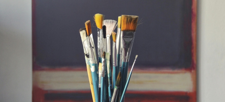 A group of paintbrushes standing in a jar in front of a canvas.