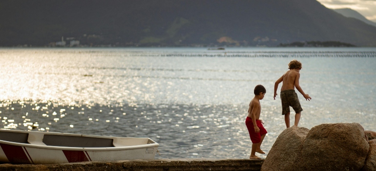Children playing near the shore, stepping across rocks with a small boat nearby.
