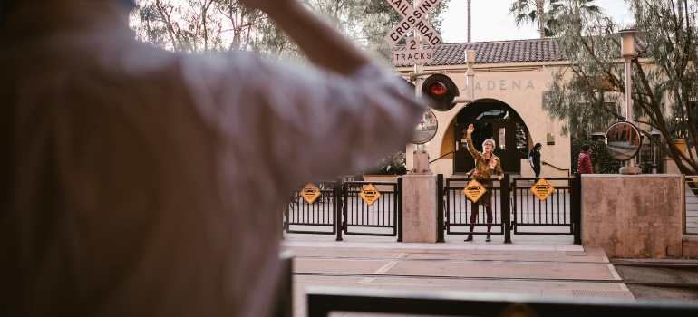 Two people waving enthusiastically across a Pasadena railroad crossing, as if reenacting a movie farewell.