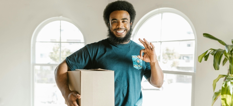 Happy mover indoors holding a box and giving an OK sign, representing moving companies Thousand Oaks.