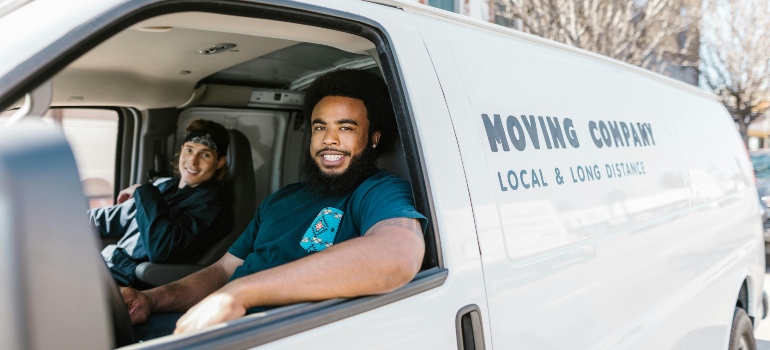 Two professional movers sitting in a moving van, smiling and ready for the job.
