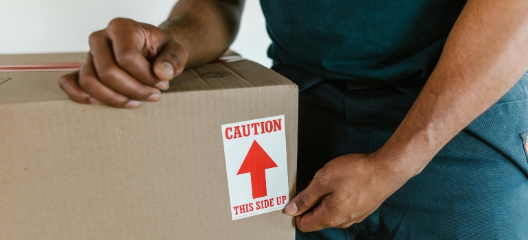 Mover carefully placing a caution sticker on a cardboard box to ensure safe handling.